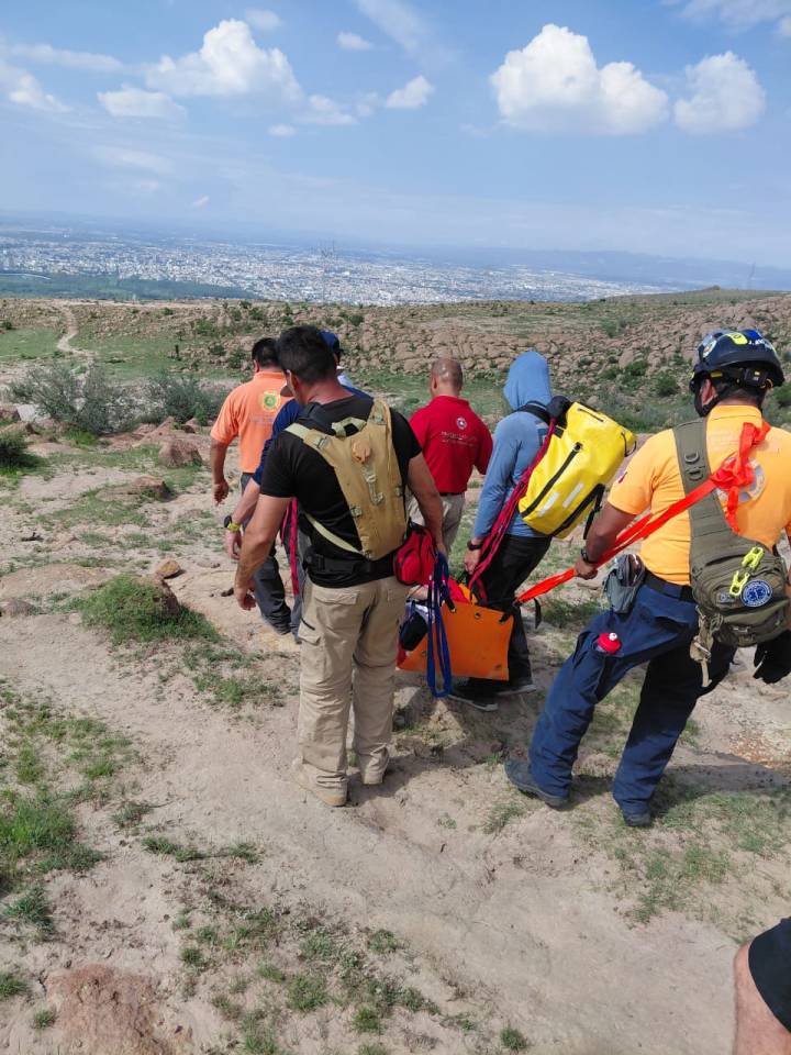 Grupo de rescatistas descendiendo una ladera en la Sierra de San Miguelito mientras transportan a un senderista en camilla.